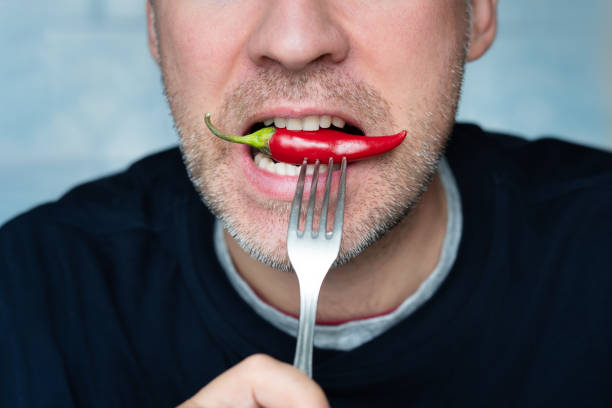 istock red pepper on a fork while eating. Portrait of young man eating chili pepper 2192129750