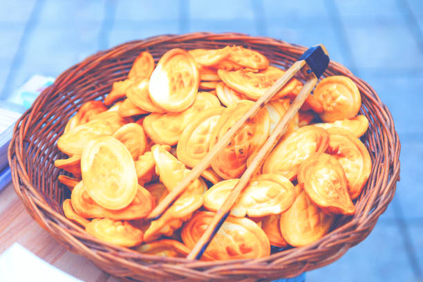 Wicker basket filled with oval shaped pastries. There is a pair of wooden tongs resting on top, suggesting the pastries are ready to be served or sold. Basket overflowing with fried dough pieces