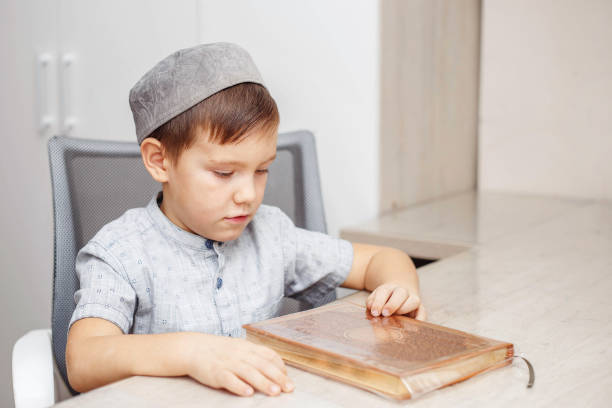 Boy sitting in mosque reading Quran. The child is sitting on the carpet under the light shining from the window of the mosque. He is reading the Quran in the lectern. worshiping. Shot with a full frame camera.