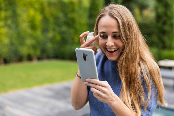 istock Smiling woman applying cream while looking at smartphone in garden 2192143489