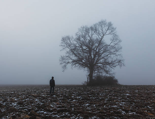 Male farmer standing on plowed agricultural field covered with fog