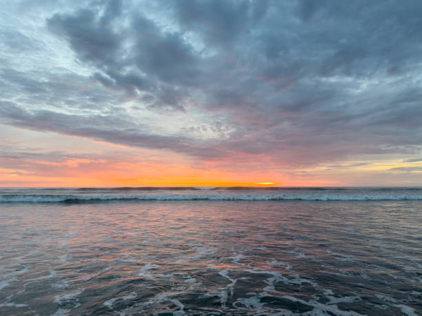 Sky painted with shades of orange, pink, and purple as sun sets over calm ocean waters, creating peaceful atmosphere.