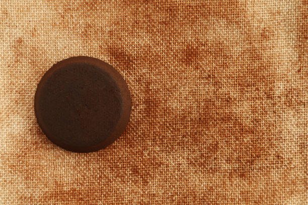 Used coffee puck placed on a textured linen fabric background, with plenty of free space around it, allowing room for text, in warm brown tones