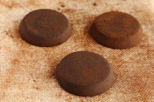 Three used coffee pucks after brewing espresso, perfectly tamped and evenly balanced, resting on a textured linen fabric background, surrounded by warm brown tones