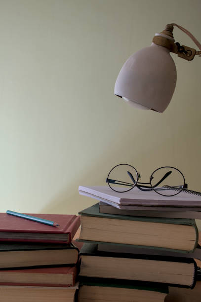 istock glasses on a stack of books on a desk with a reading lamp 2192158594