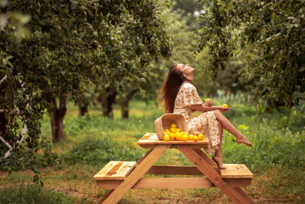 Close up photo of young beautiful stylish girl in red linen summer dress posing between peach trees. Pretty smile lady with long healthy blonde hair and fresh makeup. Summer lifestyle concept.