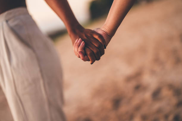 istock Close-up of a couple holding hands on a sandy beach during sunset 2192160629