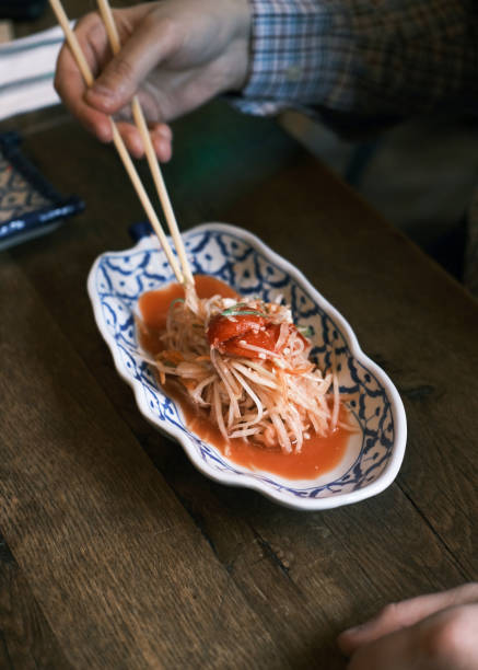 istock Authentic Thai Papaya Salad Served in a Traditional Ceramic Bowl, Garnished with Fresh Vegetables and Tangy Dressing, Enjoyed with Chopsticks in a Cozy Thai Restaurant 2192161413