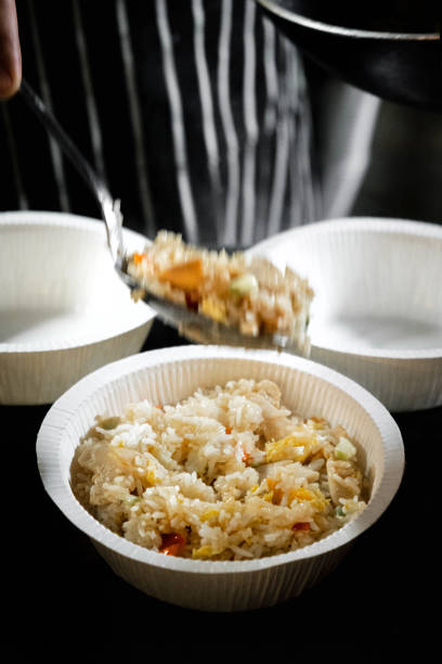 A serving of traditional Thai fried rice with chicken and fresh vegetables, presented in eco-friendly disposable bowls. The dish features perfectly cooked rice stir-fried with colorful ingredients, including carrots, onions, and cabbage, capturing the vibrant flavors of Thai cuisine. The steaming rice is served with care, emphasizing both the aroma and freshness of the dish. This image showcases a casual and convenient dining experience, ideal for takeaway or quick meals, while maintaining the authenticity of Thai culinary traditions.