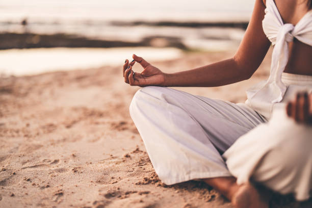 Person meditating on a sandy beach at sunset in a tranquil setting