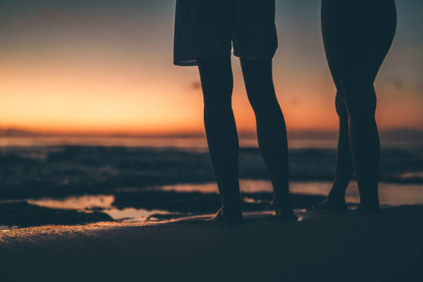Silhouettes of two people standing side by side on a beach during a dramatic sunset, evoking feelings of companionship, serenity, and reflection in a beautiful coastal setting.