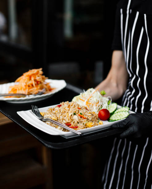 istock Thai restaurant server carrying a tray with fried rice and papaya salad, authentic Thai cuisine, freshly prepared meal, restaurant dining experience, traditional Thai flavors, Asian food presentation, gourmet Thai dish, server in black gloves, street food 2192164310