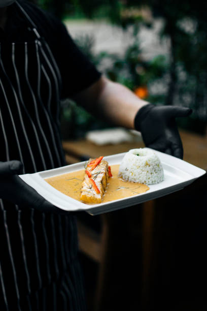Chef serving Chu Chee Curry Salmon with jasmine rice at a Thai restaurant, plated with rich coconut curry sauce, garnished with red chili, black gloves, professional presentation, fine dining ambiance