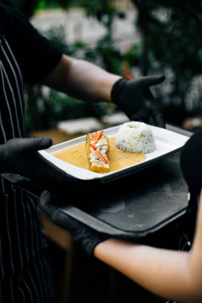istock Chef serving Chu Chee Curry Salmon with jasmine rice at a Thai restaurant, plated with rich coconut curry sauce, garnished with red chili, black gloves, professional presentation, fine dining ambiance 2192164383