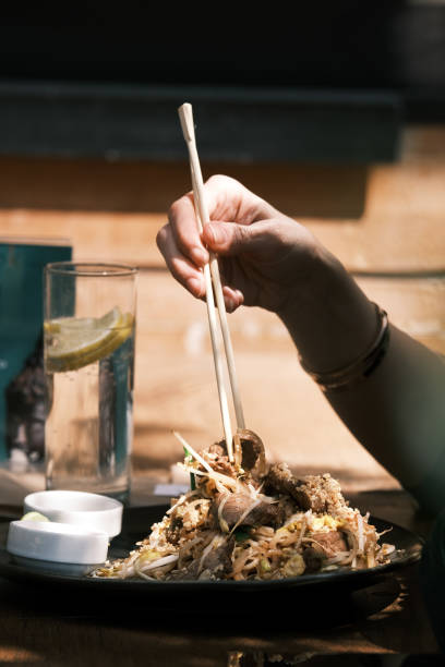 istock A diner enjoying a plate of Thai stir-fried noodles at a Thai restaurant, Using chopsticks to pick up a bite of beef and noodles, Capturing the authentic dining experience in an outdoor restaurant setting 2192164592