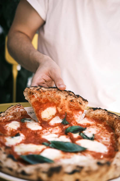 istock Neapolitan Margherita Pizza Slice with Fresh Basil, Mozzarella, and Tomato Sauce Being Hand-Picked in a Cozy Italian Restaurant, Showcasing Authentic Culinary Tradition 2192164806
