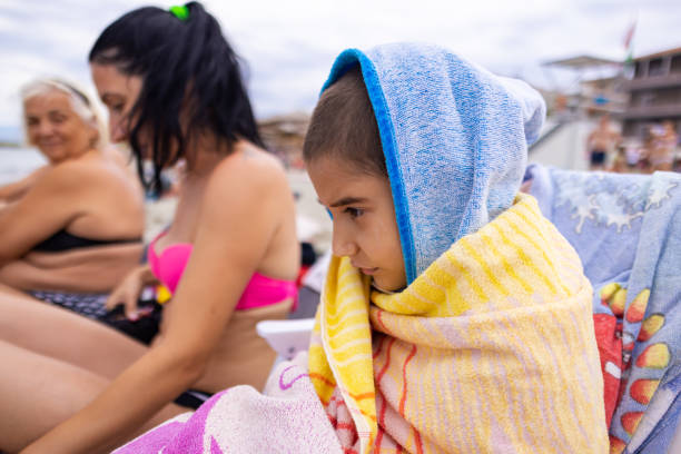 A little boy sits on the sandy beach, wrapped in a cozy towel after a refreshing swim in the sea.