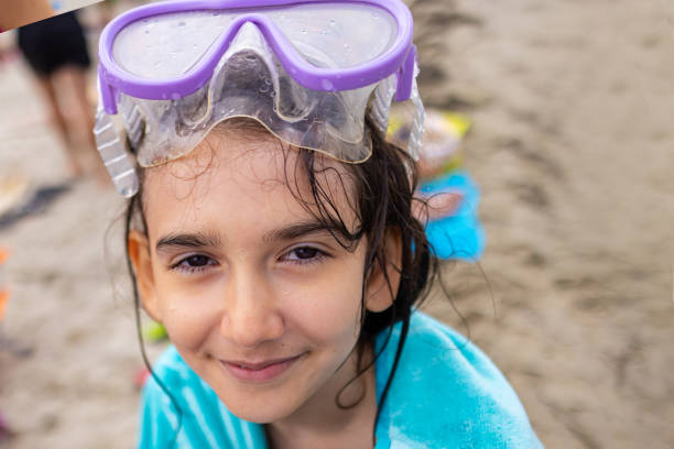 A little girl poses adorably with a blue towel around her and a purple diving mask perched on her head.