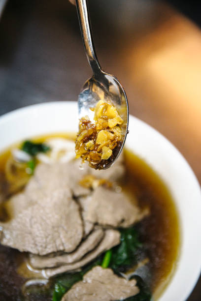 Close-up of Thai beef noodle soup with crispy garlic topping, rich broth, tender sliced beef, traditional Thai street food, authentic flavors, gourmet Asian cuisine, flavorful and aromatic soup dish