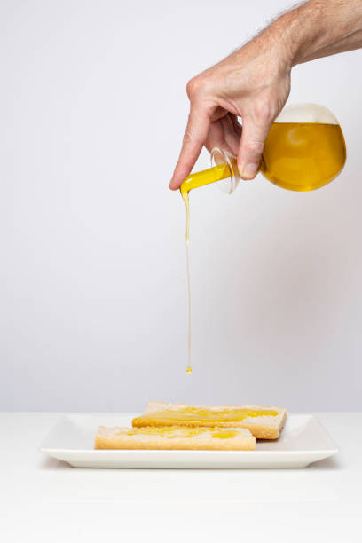 A hand drizzling extra virgin olive oil on a plate with bread. Copy space.