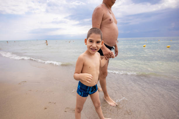 Happy father carrying his son on the neck on a tropical sand beach in summer.