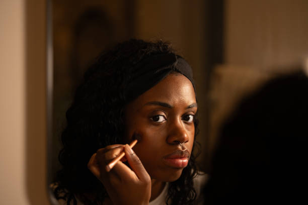 istock Woman wearing black headband applying foundation with makeup brush, looking intently into mirror, carefully preparing for evening event with focused expression 2192171465