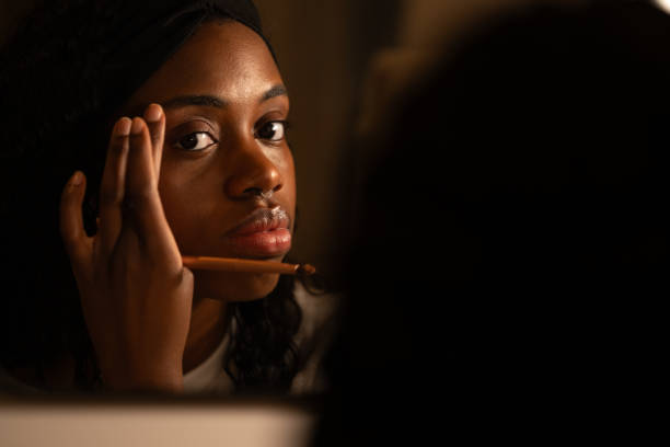 istock Black woman carefully grooming eyebrows using makeup brush, checking reflection in low-light bedroom setting before evening event 2192171490