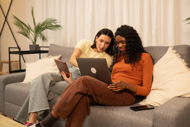 istock Young women working remotely, sharing living room sofa, using laptop and tablet while collaborating comfortably and connecting professionally 2192171735