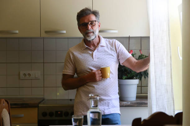istock Senior casual man drinking in his kitchen and looking outside 2192174107