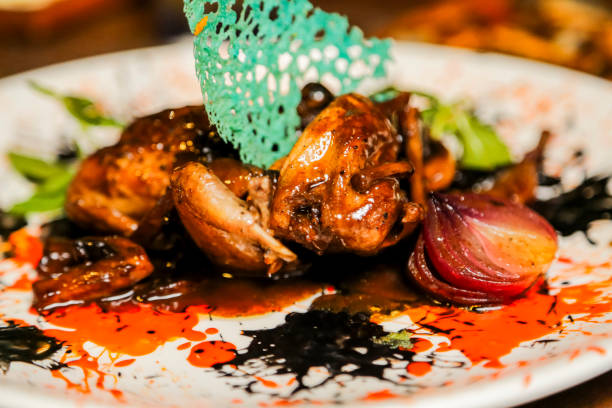 A beautifully crafted plate of quail is presented with colorful sauces, garnishes, and roasted vegetables, perfect for an upscale dining experience.