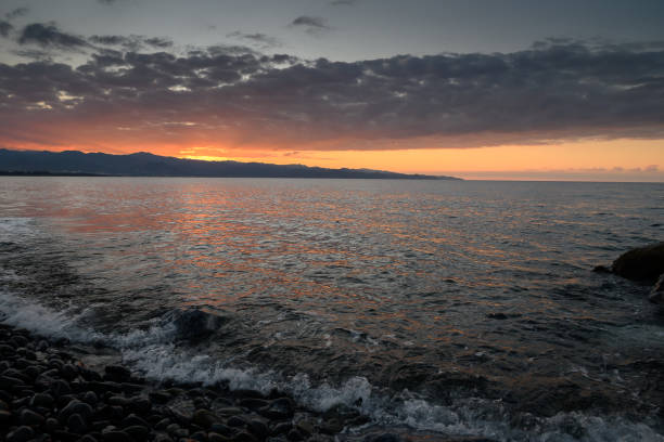 Sunset over tranquil waters creates a serene atmosphere along the rocky shoreline