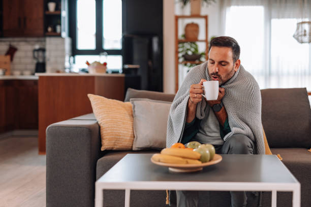 istock Sick man drinking hot tea on the sofa, covered with a blanket 2192181364