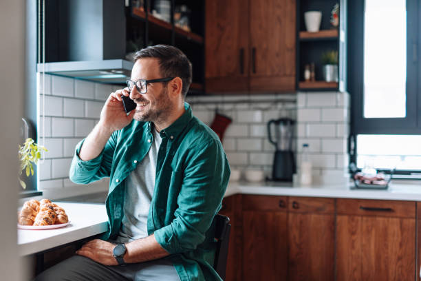 istock Happy man talking on the phone and having breakfast in the kitchen 2192181480
