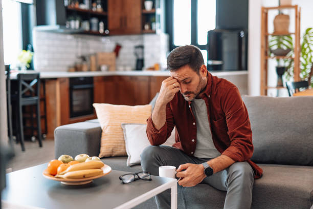 istock Stressed man sitting on sofa touching his forehead and holding a cup of coffee 2192181562