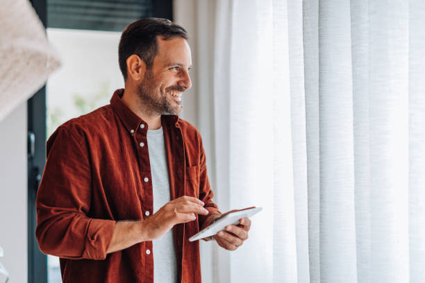 Man smiling and using digital tablet near window at home