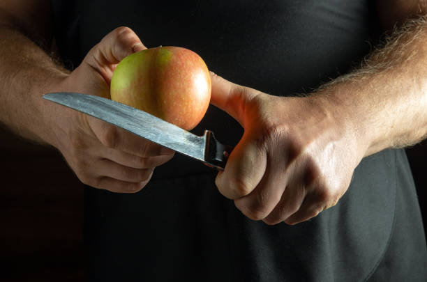 istock A pair of strong hands holds a shiny red apple while expertly gripping a gleaming knife. The warm, dim light creates an inviting atmosphere, enhancing the concentration on food preparation 2192183748