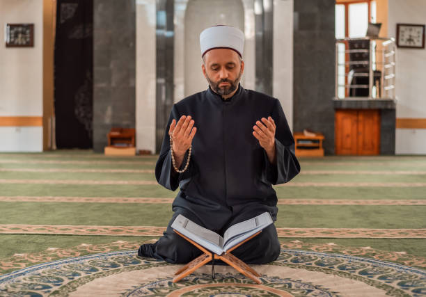 istock A Muslim prayer man praying with hands up while reading a Quran inside the mosque. 2192184227