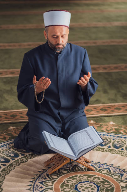 istock A Muslim prayer man praying with hands up while reading a Quran inside the mosque. 2192185636