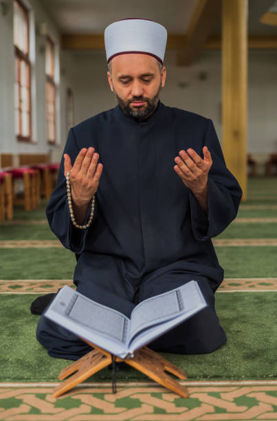 istock A Muslim prayer man praying with hands up while reading a Quran inside the mosque. 2192185684