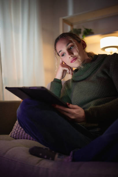 istock Young woman reading a digital tablet on the sofa at night 2192191195