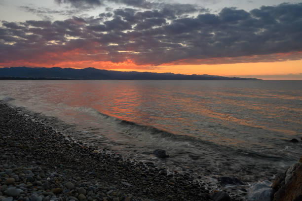istock Sunset over calm waters with rocky shore and distant mountains creating a serene evening atmosphere 2192192035