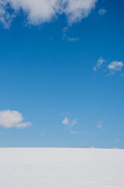 Snowy field with blue sky and white clouds in winter season.