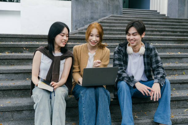 istock Three young adult students are sitting on university steps, engaged in a collaborative project using a laptop, sharing ideas and working together 2192206084
