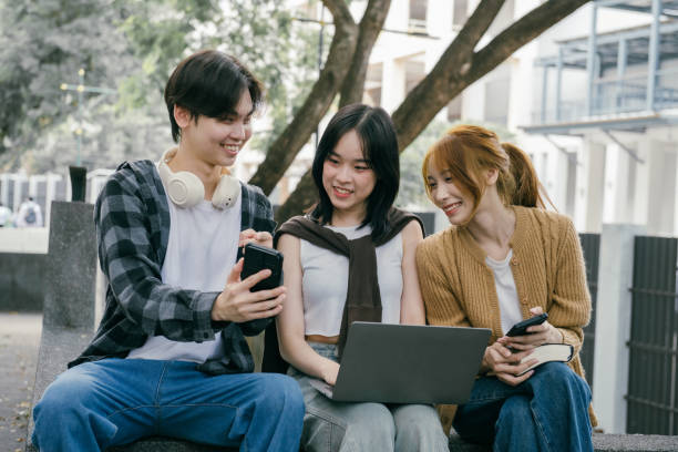 istock Three young adult students sitting outdoors, sharing smiles while using a laptop and smartphones, enjoying a moment of connection and collaboration in a vibrant campus setting 2192207133