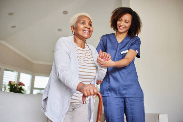 Supporting Steps: Caregiver and Senior Woman Warm scene of a caregiver assisting an elderly woman with a cane. Both are smiling, creating a heartwarming and supportive atmosphere indoors. personal care aid stock pictures, royalty-free photos & images