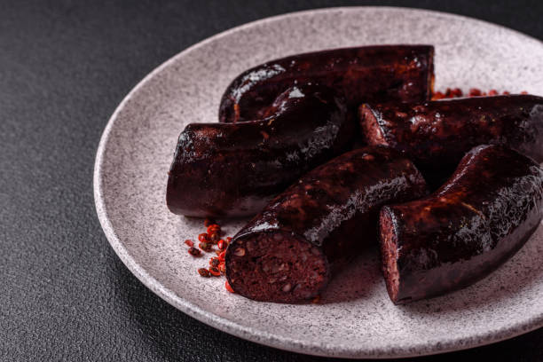 Delicious black blood sausage or black pudding with spices and herbs Delicious black blood sausage or black pudding with spices and herbs grilled on a black concrete background bloody money stock pictures, royalty-free photos & images
