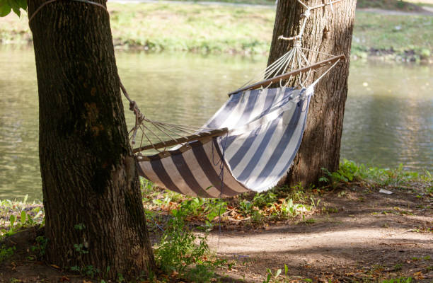 A man takes a nap in a hammock next to a crystal clear stream.