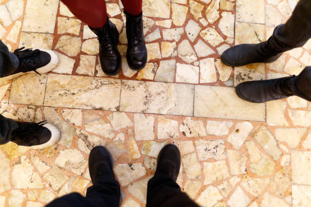 A group of people standing on a tiled floor. The floor is made of stone and the people are wearing black shoes