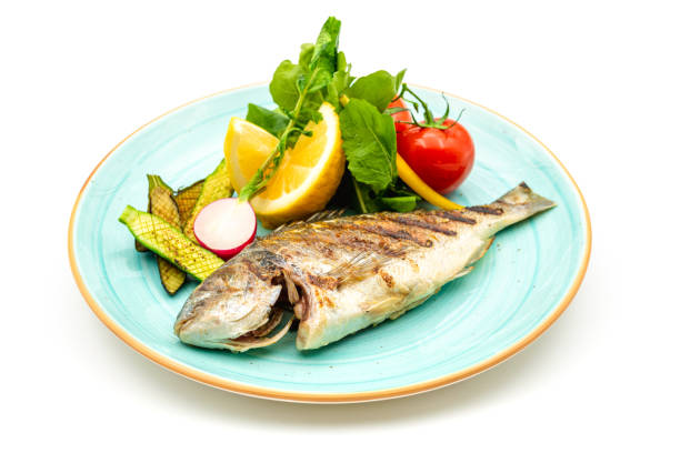 Grilled sea bream with vegetables and greens on white background