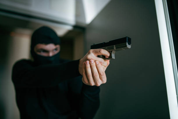 Armed robbery in house. Male thief wearing mask and holding pistol breaks into a house.